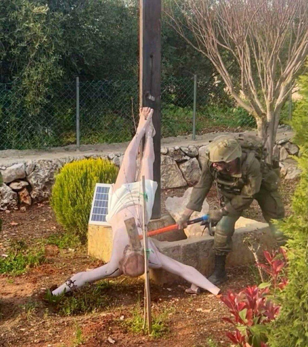 Un soldado israelí golpea con un mazo una figura escultórica de Jesucristo en un jardín