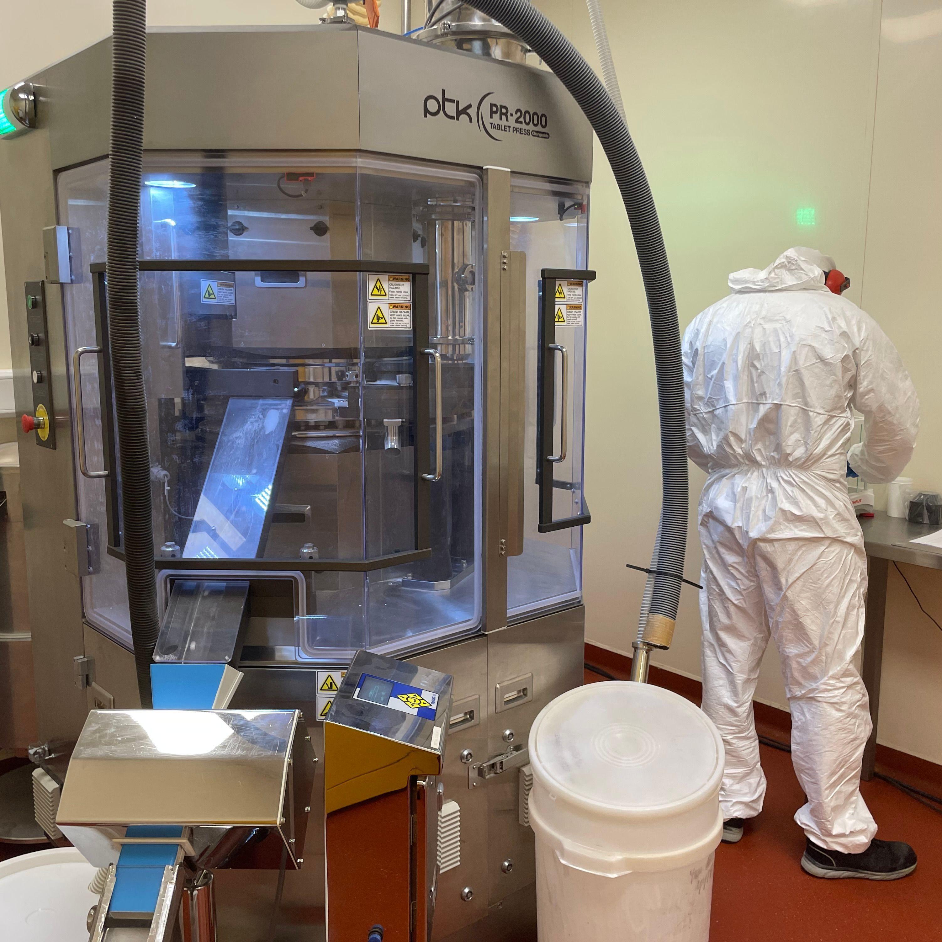 آلة ضغط الحبوب التي تحول المسحوق إلى أقراص. عامل يرتدي سترة واقية بيضاء بجانب الآلة المعدنية.