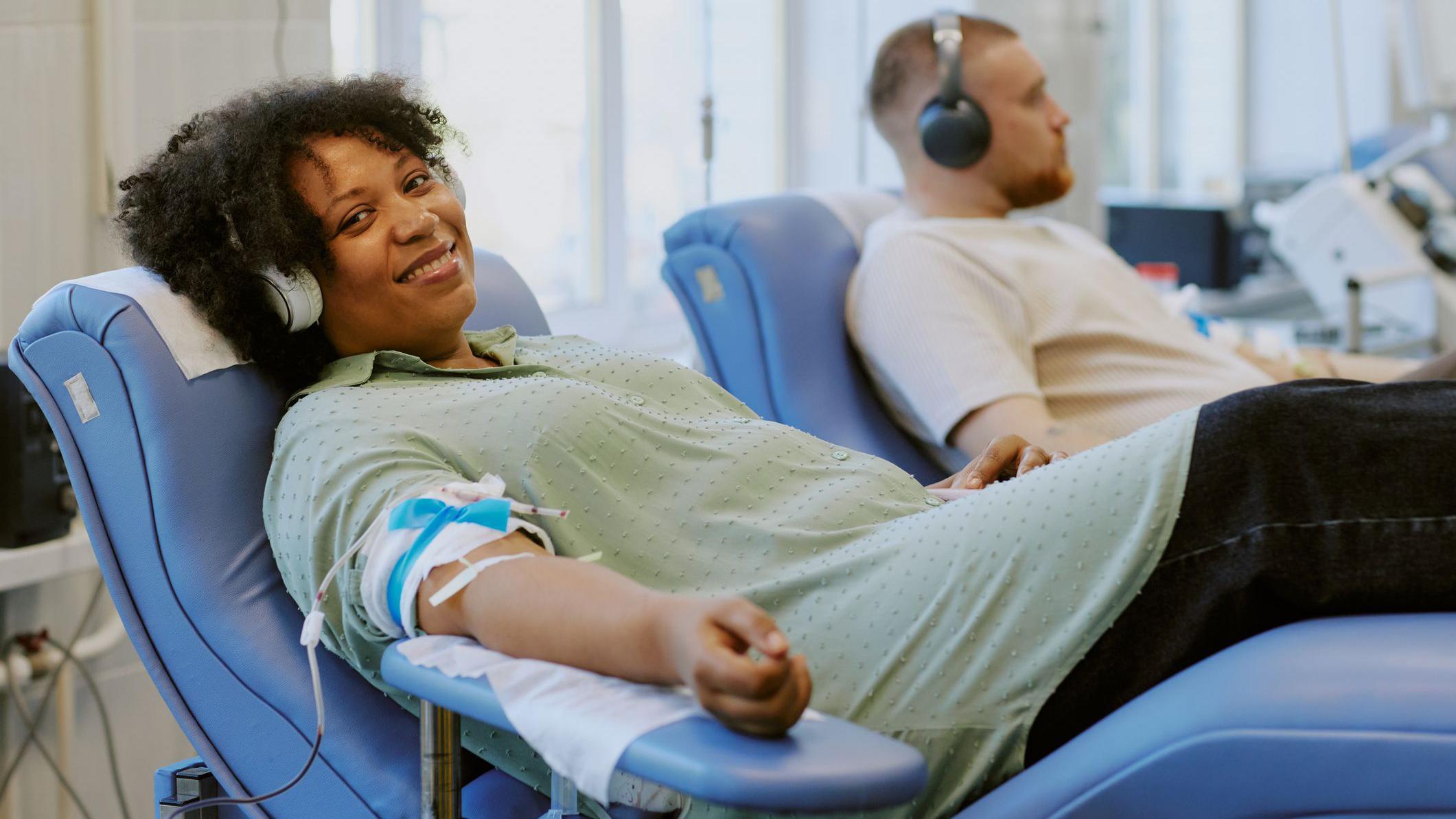 Mulher afro-americana e homem caucasiano doam sangue, relaxados sobre cadeiras reclináveis
