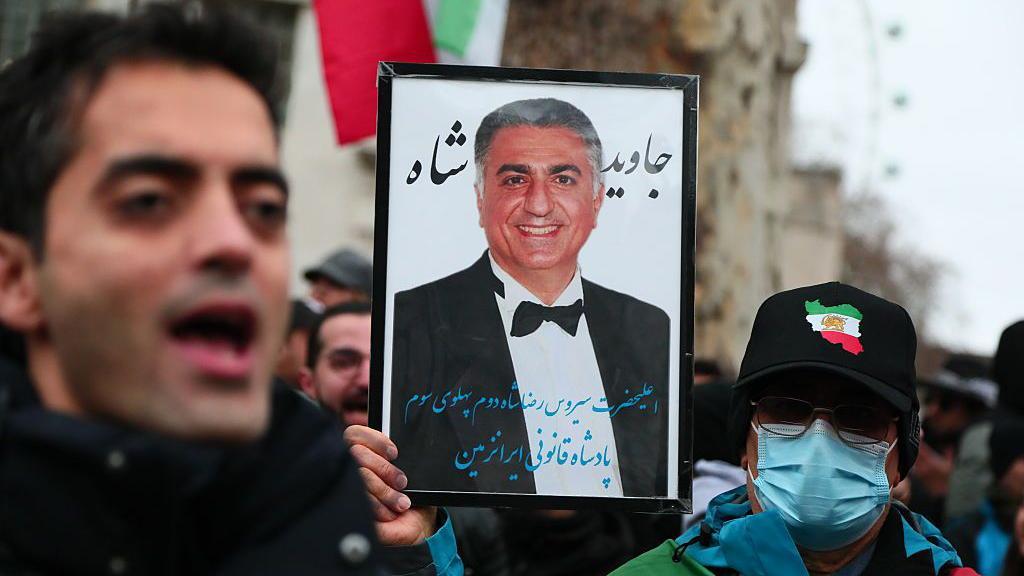 2026年1月11日，在英國倫敦，人們舉著伊朗末代國王之子、流亡的禮薩·巴列維的照片。