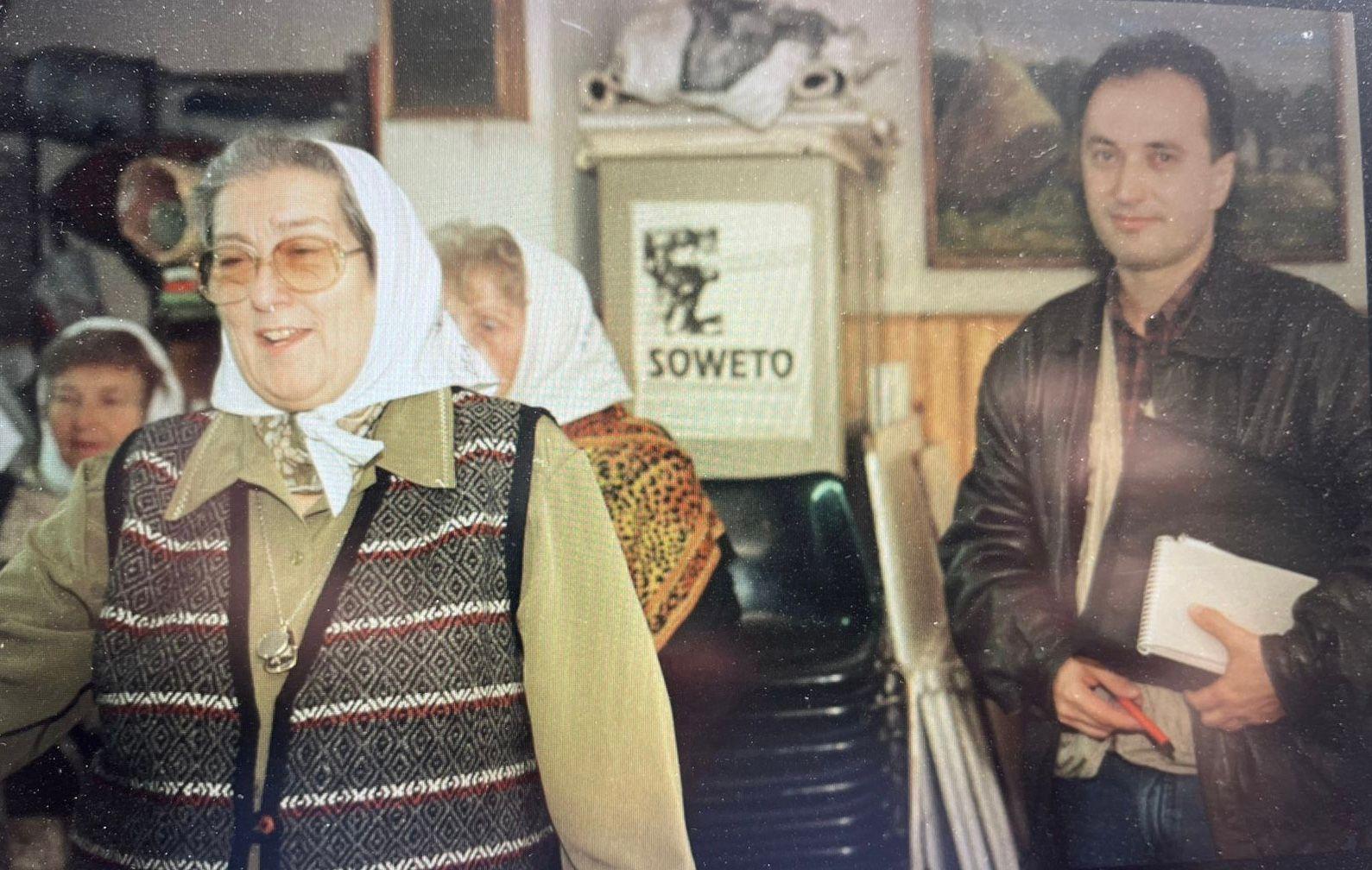 Uma mulher usando &oacute;culos e sorrindo. Ao lado dela est&aacute; Nilson Mariano