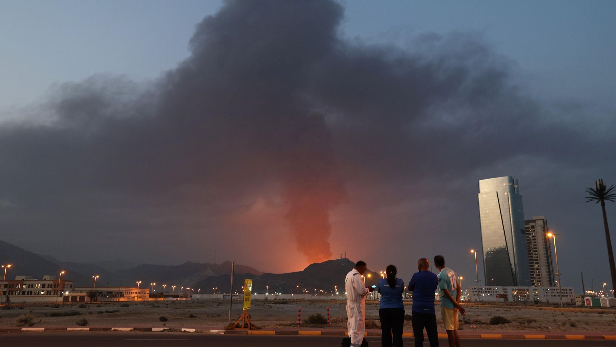 صورة من الأعلى - عمال أجانب ينظرون إلى عمود كثيف من الدخان الأسود يتصاعد عقب انفجار في المنطقة الصناعية بالفجيرة في 3 مارس/آذار 2026. أجبرت الغارات الإيرانية على دول الخليج المجاورة منذ 28 فبراير/شباط، عقب الهجوم الأمريكي الإسرائيلي، الإمارات العربية المتحدة على إغلاق مجالها الجوي، مما فاجأ المسافرين الذين ظنوا أنهم متجهون إلى واحدة من أكثر الوجهات السياحية أمانًا في المنطقة.
