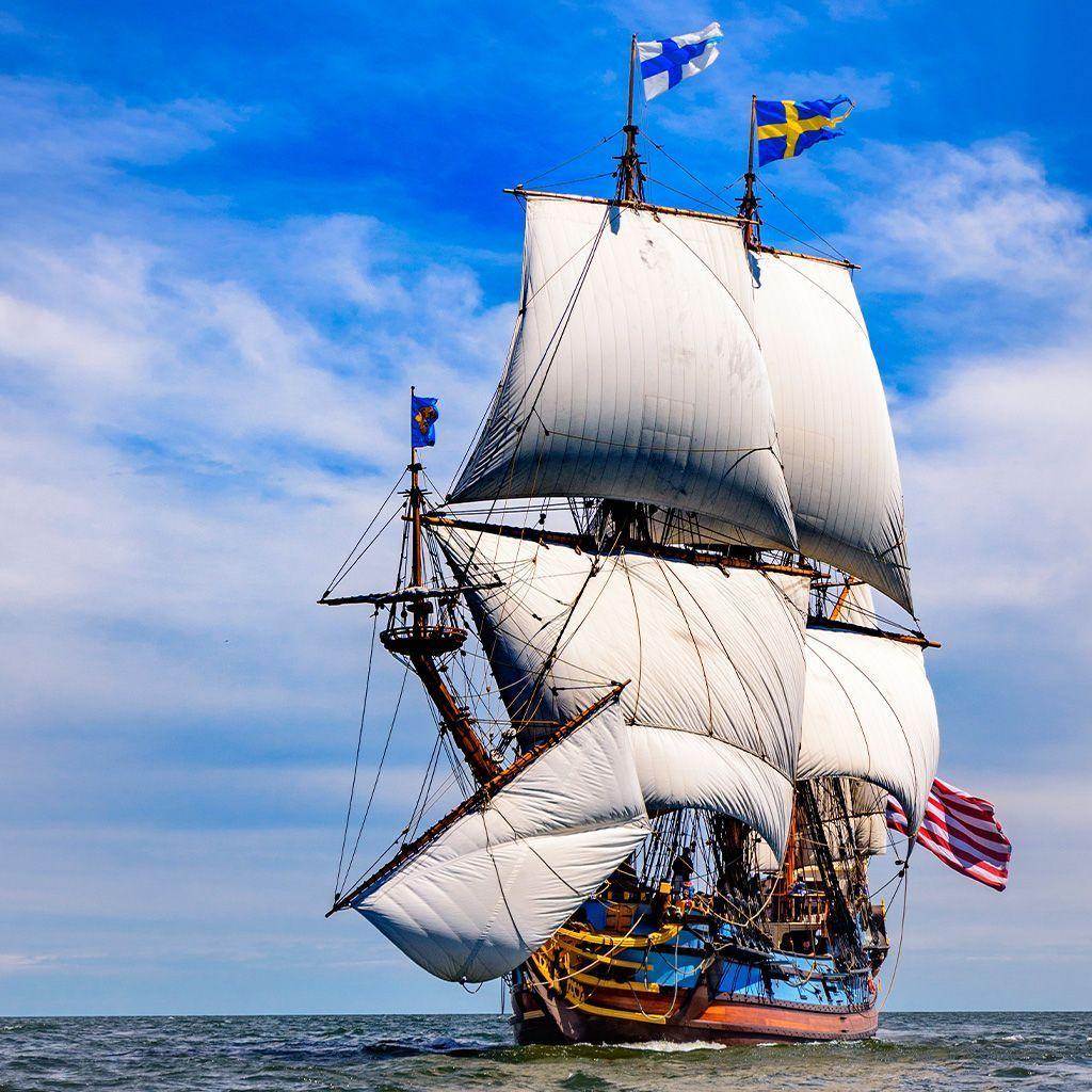 Réplica de un barco a vela histórico, el Kalmar Nyckel, con velas desplegadas en mar abierto y banderas de Suecia ondeando en lo alto de sus mástiles.
