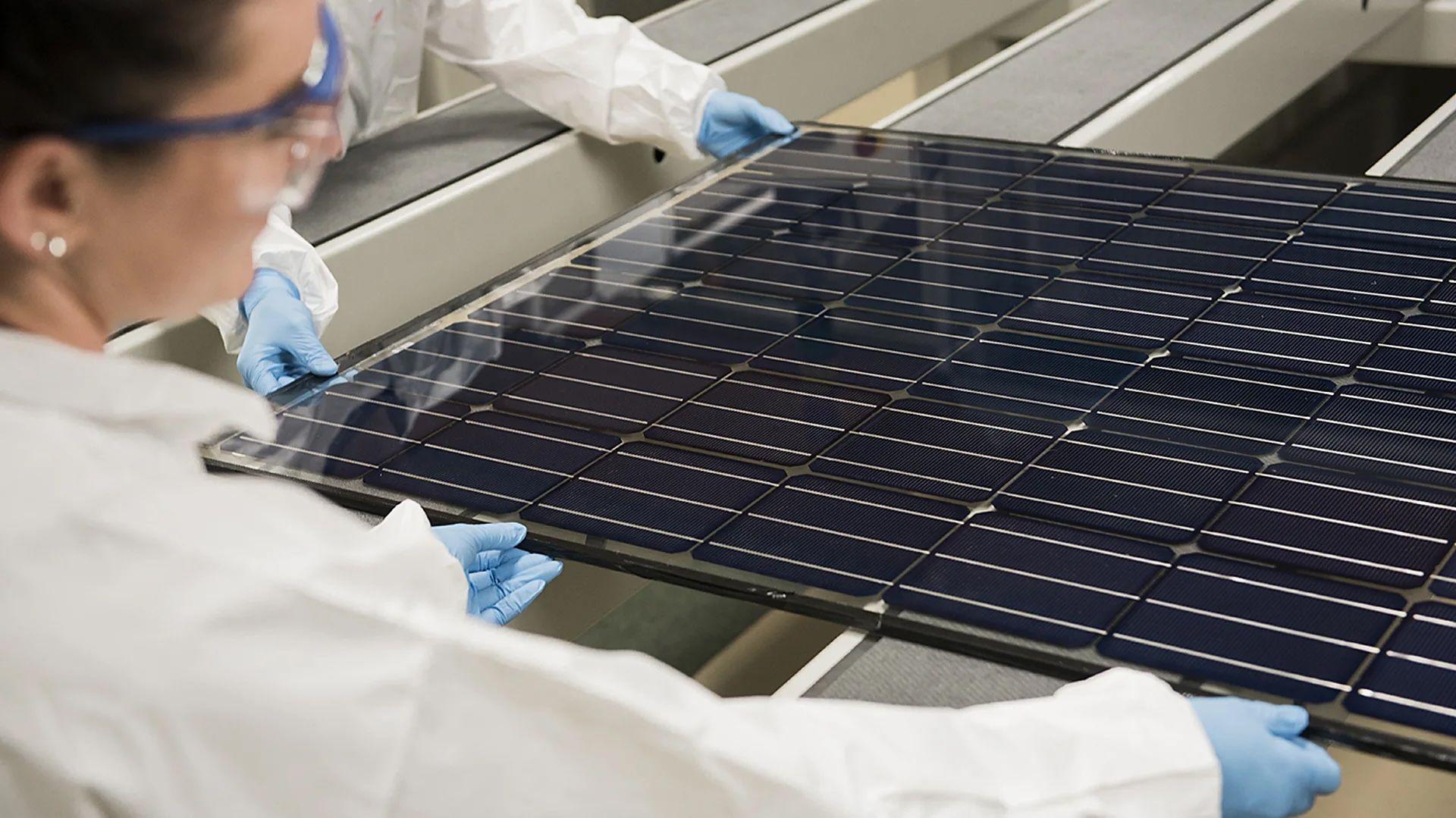 Dos investigadores con batas blancas y guantes de látex colocan un panel solar sobre una superficie 