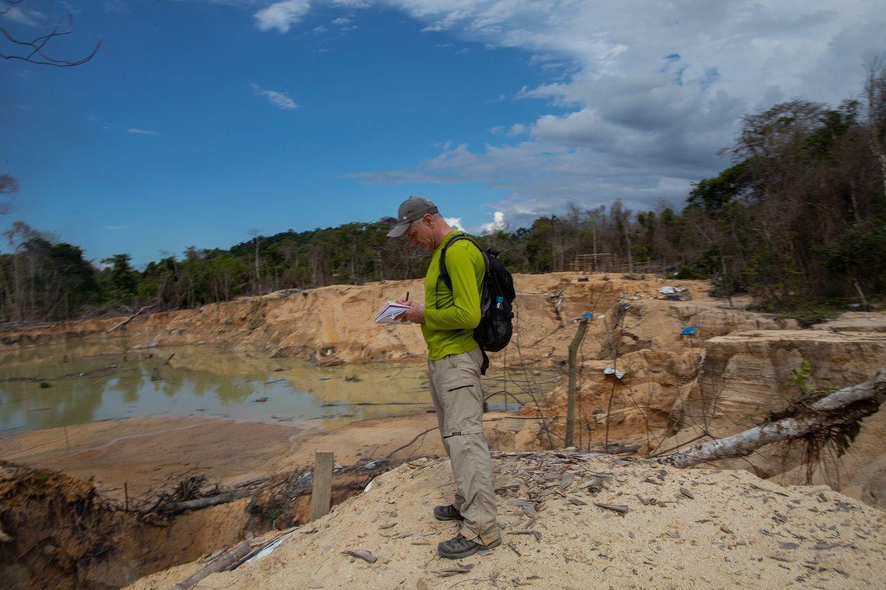 Dom anotando algo em bloco em área aberta, com areia e água