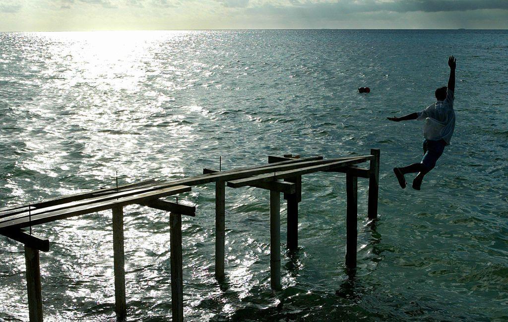 Hombre lanzandose desde un muelle cubierto de agua.
