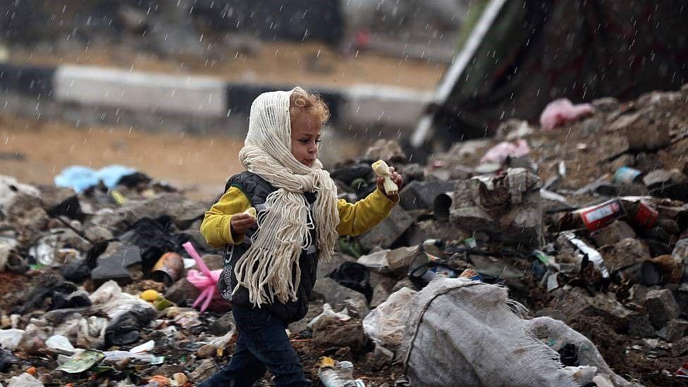 Un niño con bufanda y gorro corre entre un vertedero de desechos