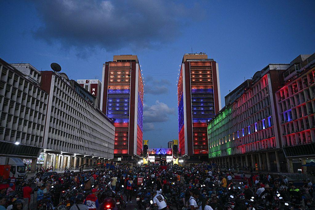 تظهر الصورة جموعاً غفيرة من المتظاهرين، بينما تضاء الأبنية المحيطة بهم بألوان العلم الفنزويلي. الصورة التقطت في المساء.