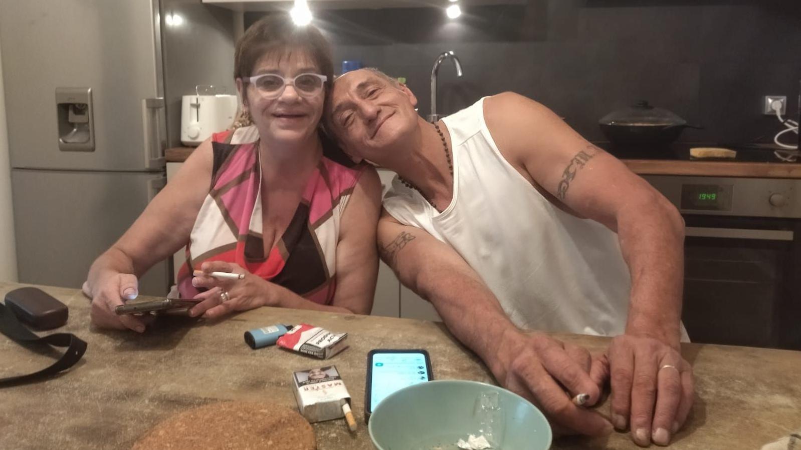 Andrea y Alejo están sentados en una cocina. Cada uno sostiene un cigarrillo, y ella, un celular. En la encimera se ve otro teléfono, un par de cajetillas de cigarrillos, un plato que hace las veces de cenicero y el estuche de unas gafas. Alejo recuesta su cabeza en el hombro de Andrea mientras miran a la cámara.