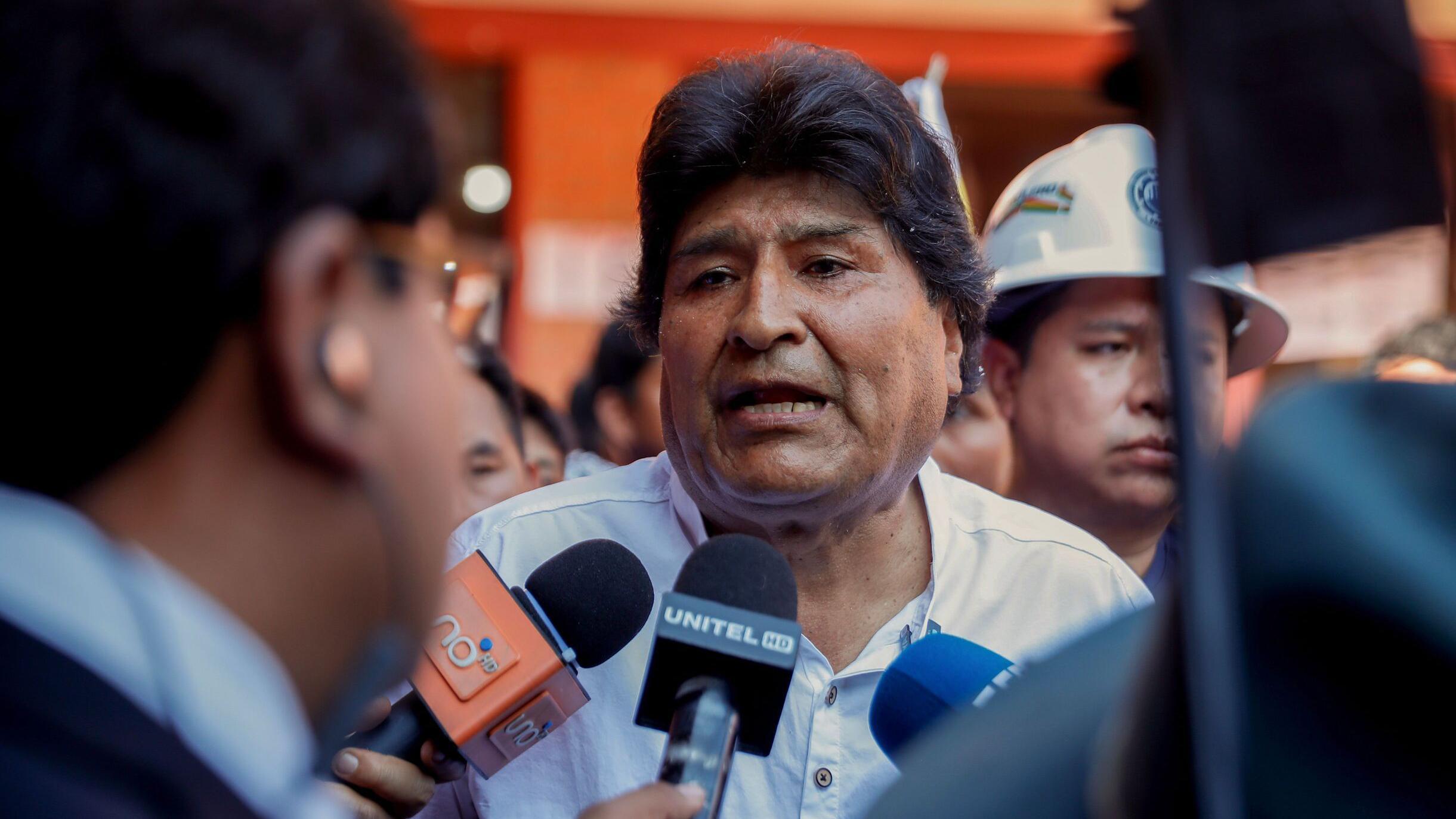 Evo Morales respondiendo a la prensa, tiene dos micrófonos delante. Detrás hay un hombre con casco de obra y otras personas a las que apenas se ve.