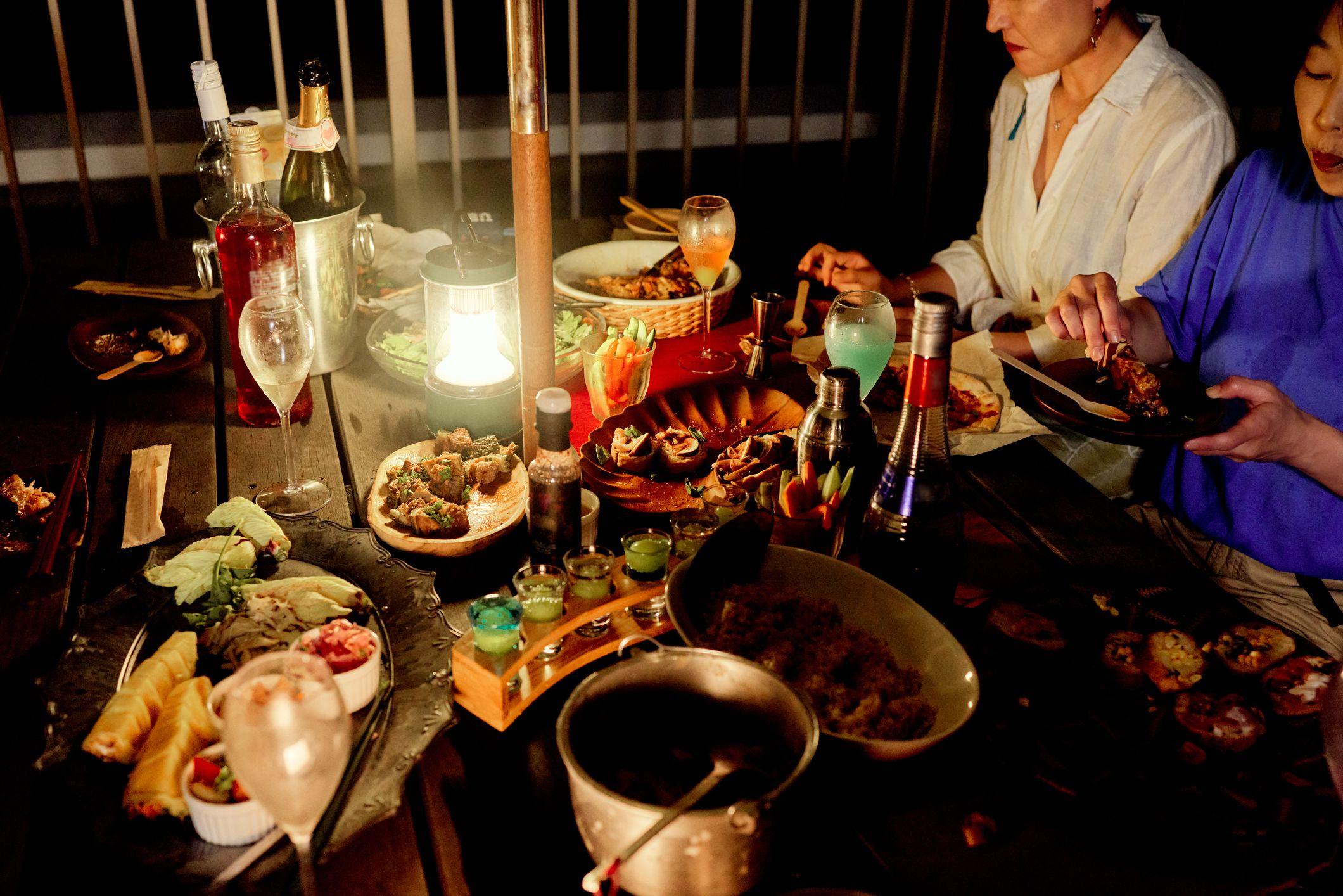Una mesa con distintos platos en la noche y un grupo de amigos que se reunió a cenar.