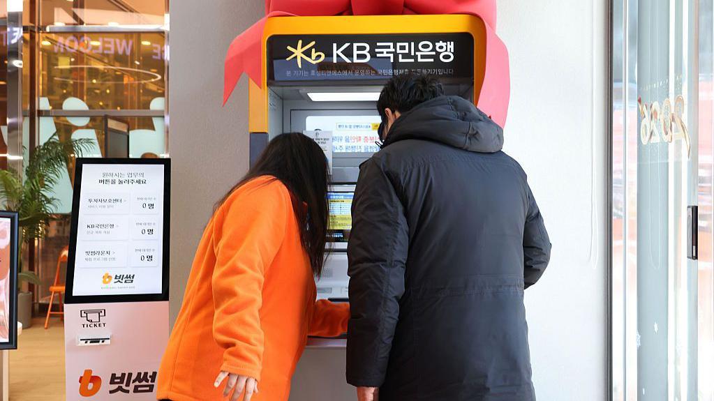 Clientes utilizan un cajero automático de KB Kookmin Bank ubicado dentro de una sucursal con señalización de Bithumb.