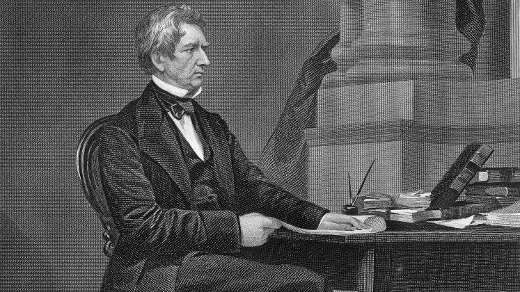 Un dibujo del secretario de Estado estadounidense, William Seward, quien negoció la compra de Alaska. Es en blanco y negro y muestra a un hombre sentado en una silla cerca de un escritorio. El hombre viste un elegante traje oscuro y apoya una mano en el escritorio. En el escritorio hay libros y papeles.
