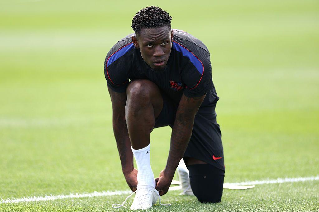 Falorin Balogun, arrodillado calzándose una bota en un entrenamiento de EE.UU. 