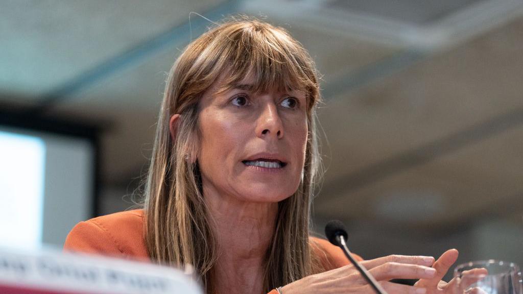 primer plano de begoña gómez, habla frente a un micrófono, está sentada y mueve las manos hacia el frente. 