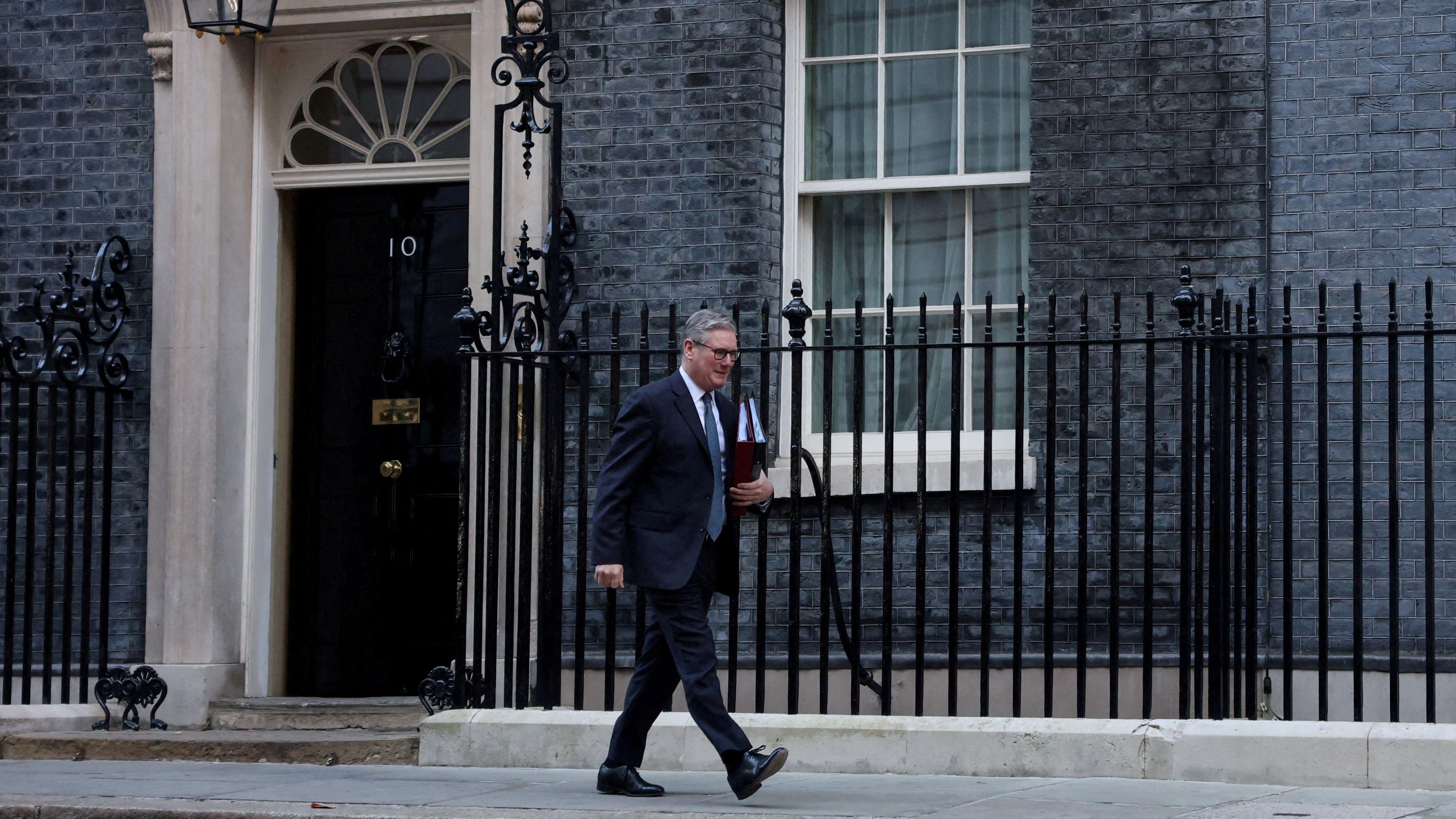 施紀賢爵士步出倫敦唐寧街10號首相府後往街口走去，左手抱著兩個文件夾（26/11/2025）