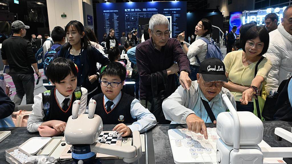 2025年12月19日：在香港會議展覽中心舉行的首屆香港人工智慧藝術節上，老年人（右）和學生們與人工智慧機器人下棋。