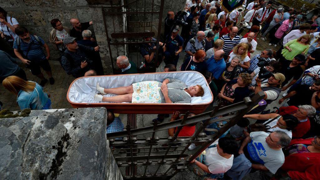 Mulher sendo levada em um caixão aberto durante a romaria