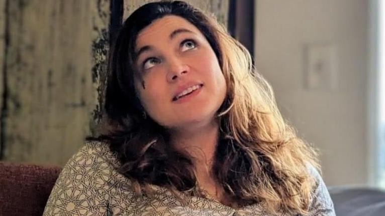 سيدة ذات شعر بني فاتح تجلس على أريكة وتنظر إلى أعلى