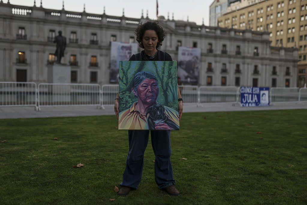 Una mujer posa con el retrato de Julia Chuñil al frente de la casa de gobierno en Santiago de Chile. 
