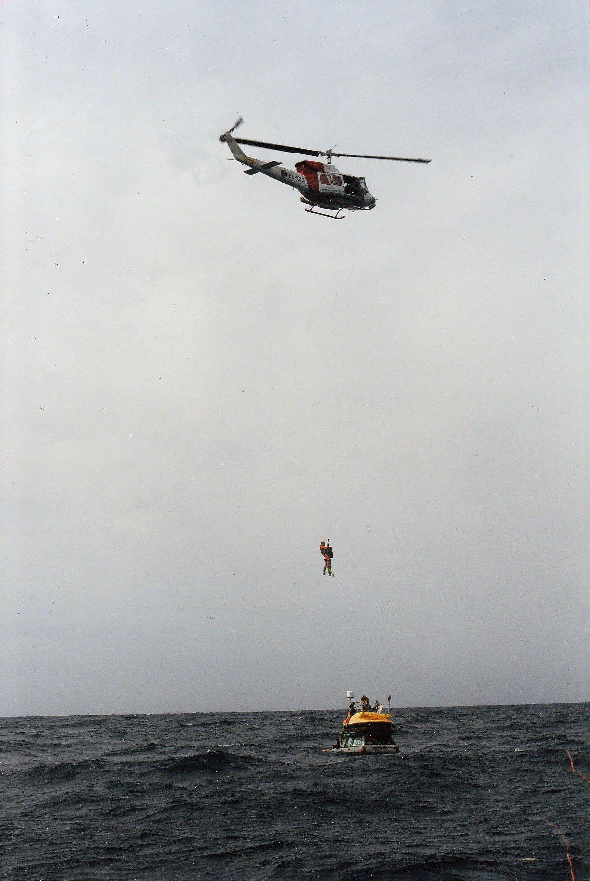 Un helicóptero se mantiene en vuelo estacionario sobre los coches en el mar, izando a dos hombres hasta un lugar seguro.