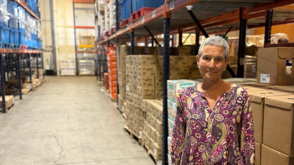 Nelle Miller en un almacén delante de grandes estantes con cajas con productos.