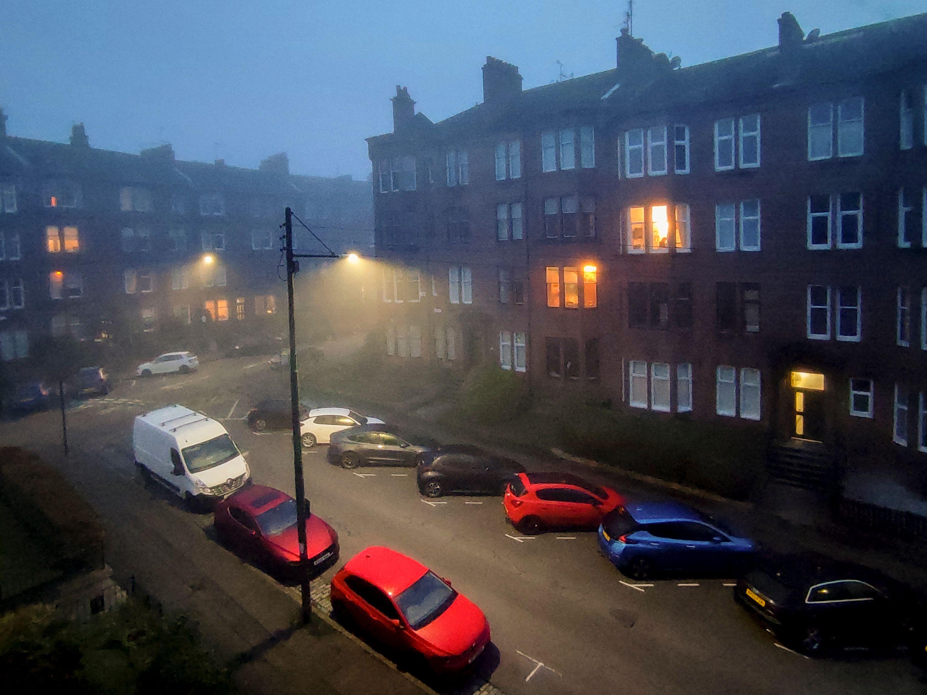 Una foto de una calle brumosa de Glasgow, con varios carros estacionados.