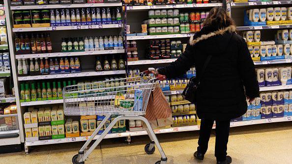 Mulher olha para g&ocirc;ndola de supermercado enquanto segura um carrinho com uma das m&atilde;os
