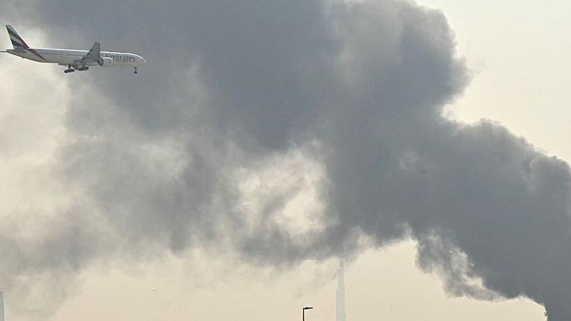 صورة تُظهر طائرة تابعة للخطوط الجوية الإماراتية وهي تطير بمحاذاة دخان أسود كثيف بالقرب من مطار دبي.