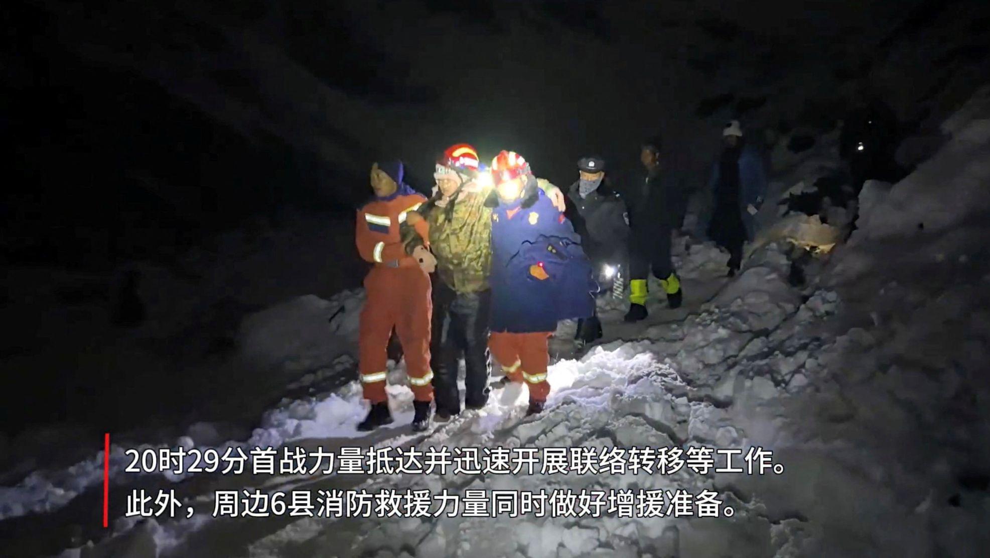Una senderista con casco y ropa térmica se apoya en dos socorristas mientras bajan una ladera llena de nieve durante la noche, seguidos de otros tres socorristas, uno de los cuales ilumnina el camino con una lámpara.