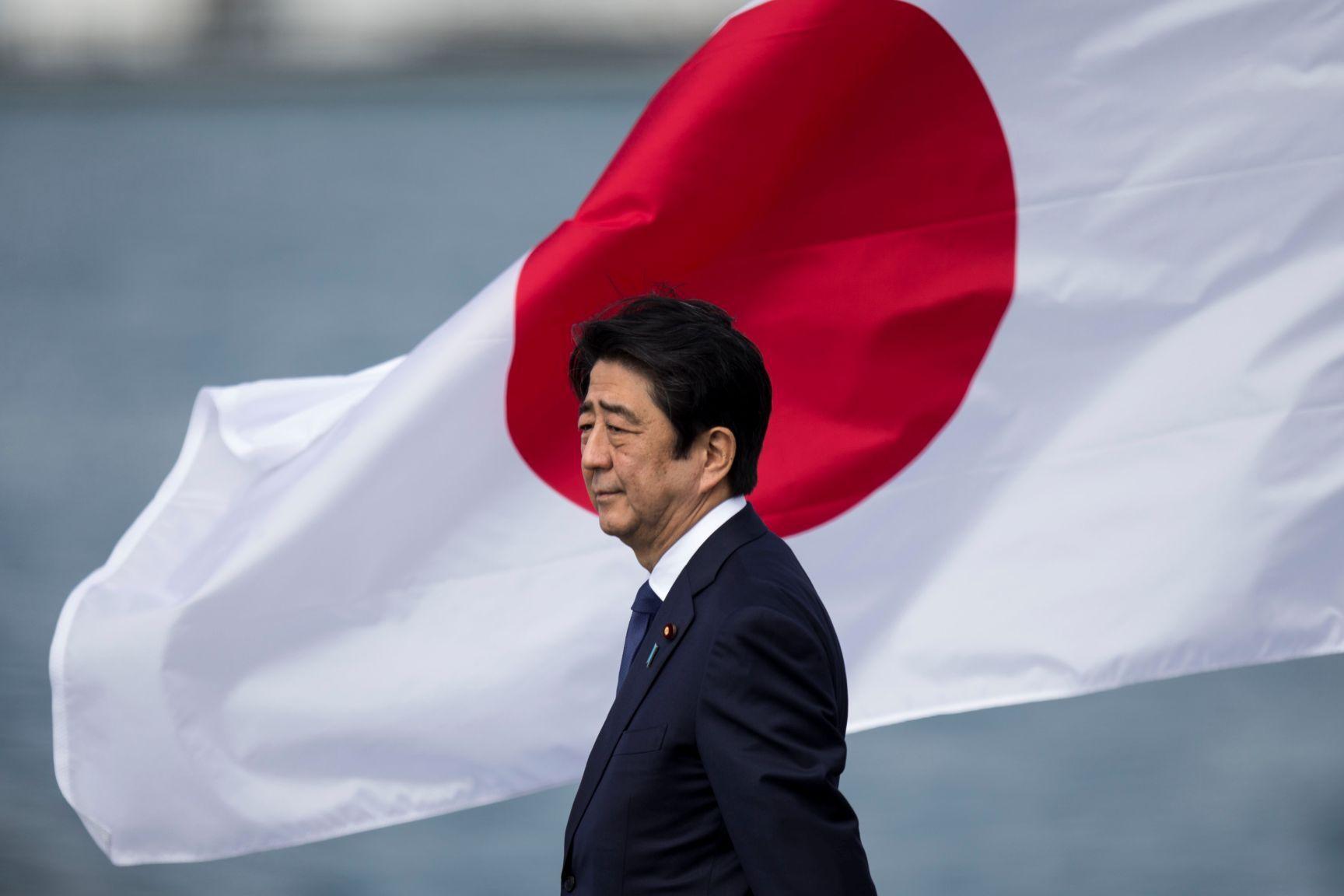 Shinzo Abe com a bandeira do Japão ao fundo