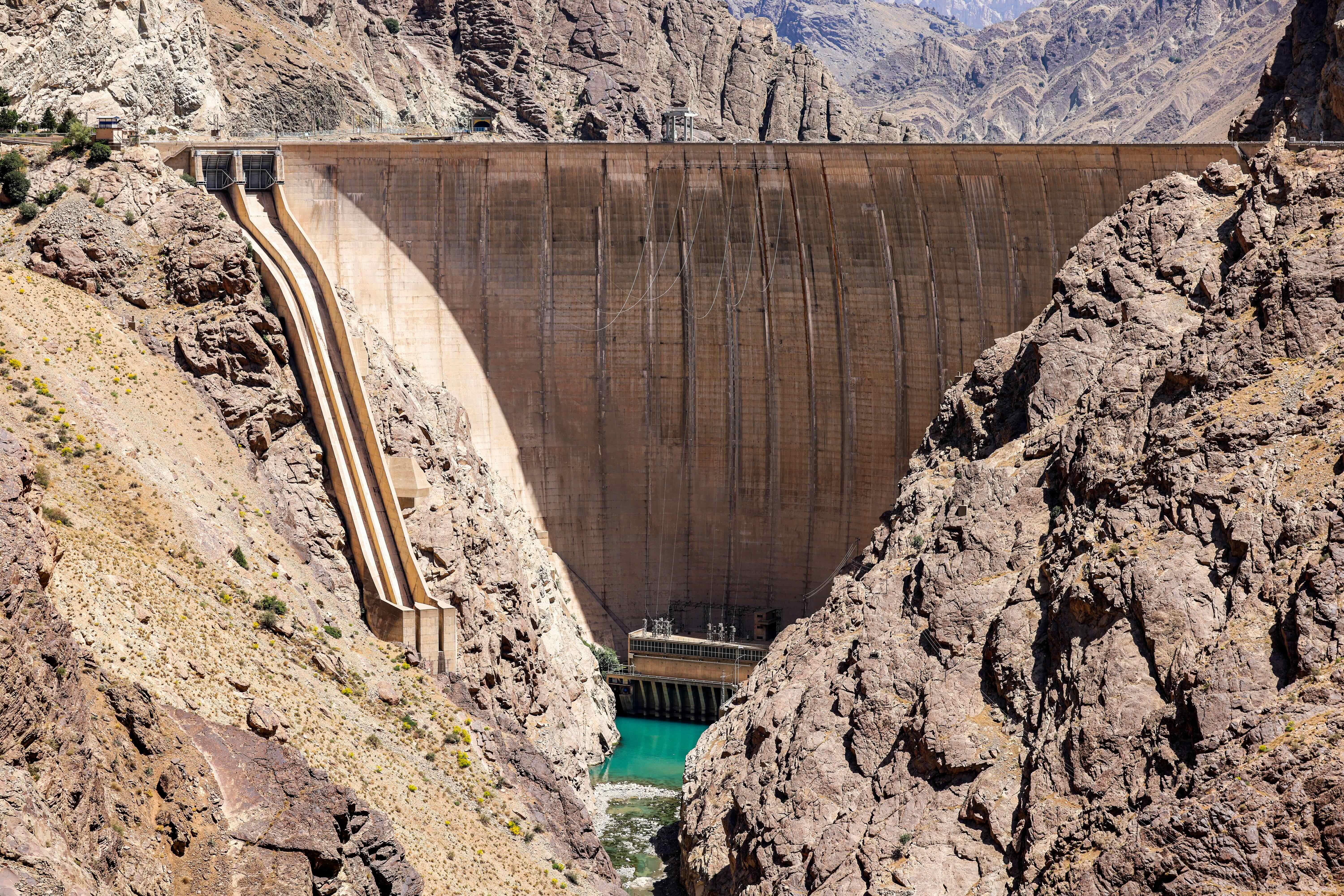 A reservoir with low water level can be seen between rocks, with the wall of the Amir Kabir Dam towering over the water expanse