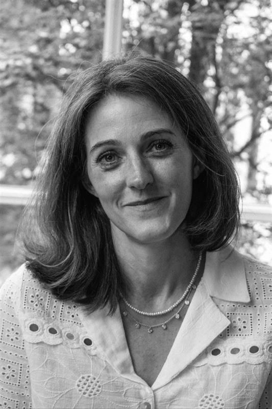 Crno-bela fotografija Ejmi Dikson koja gleda u kameru, ima belu blizu i ogrlice