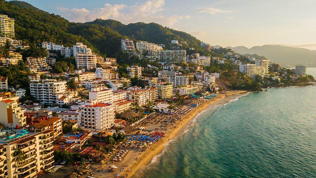 Praia de Puerto Vallarta, no M&eacute;xico, com pr&eacute;dios e morros ao fundo