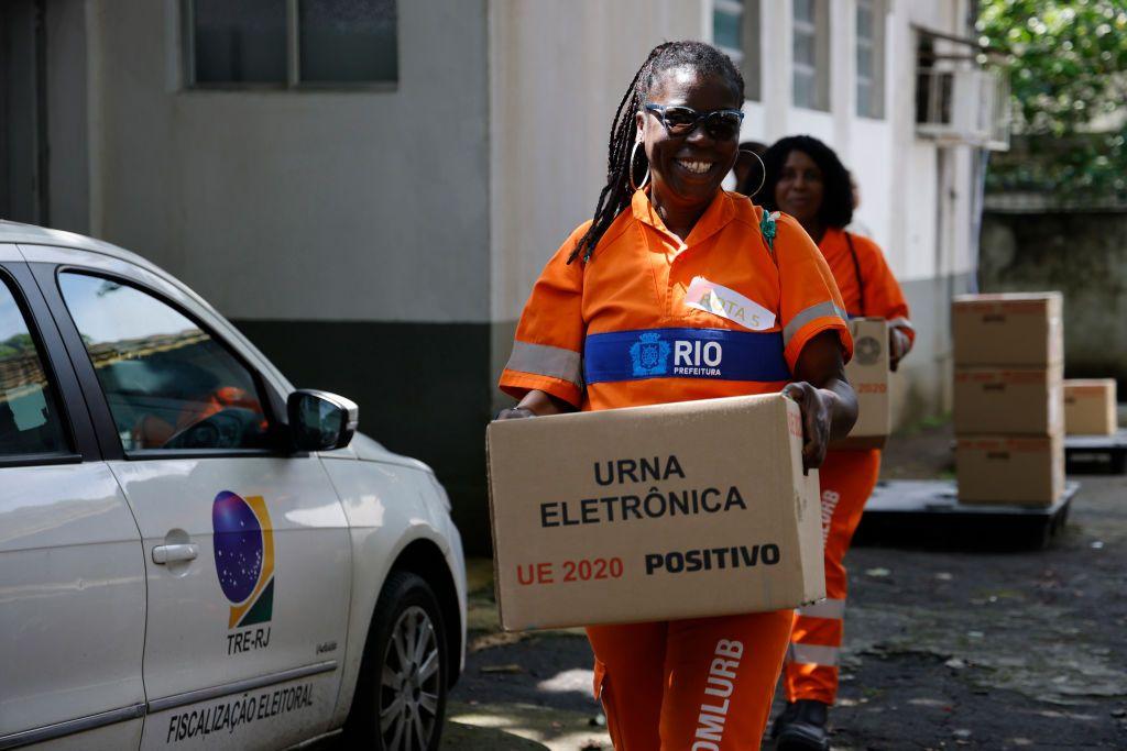 Una mujer vestida con un uniforme de la alcaldía de Río de Janeiro sostiene una caja que dice "urna electrónica".