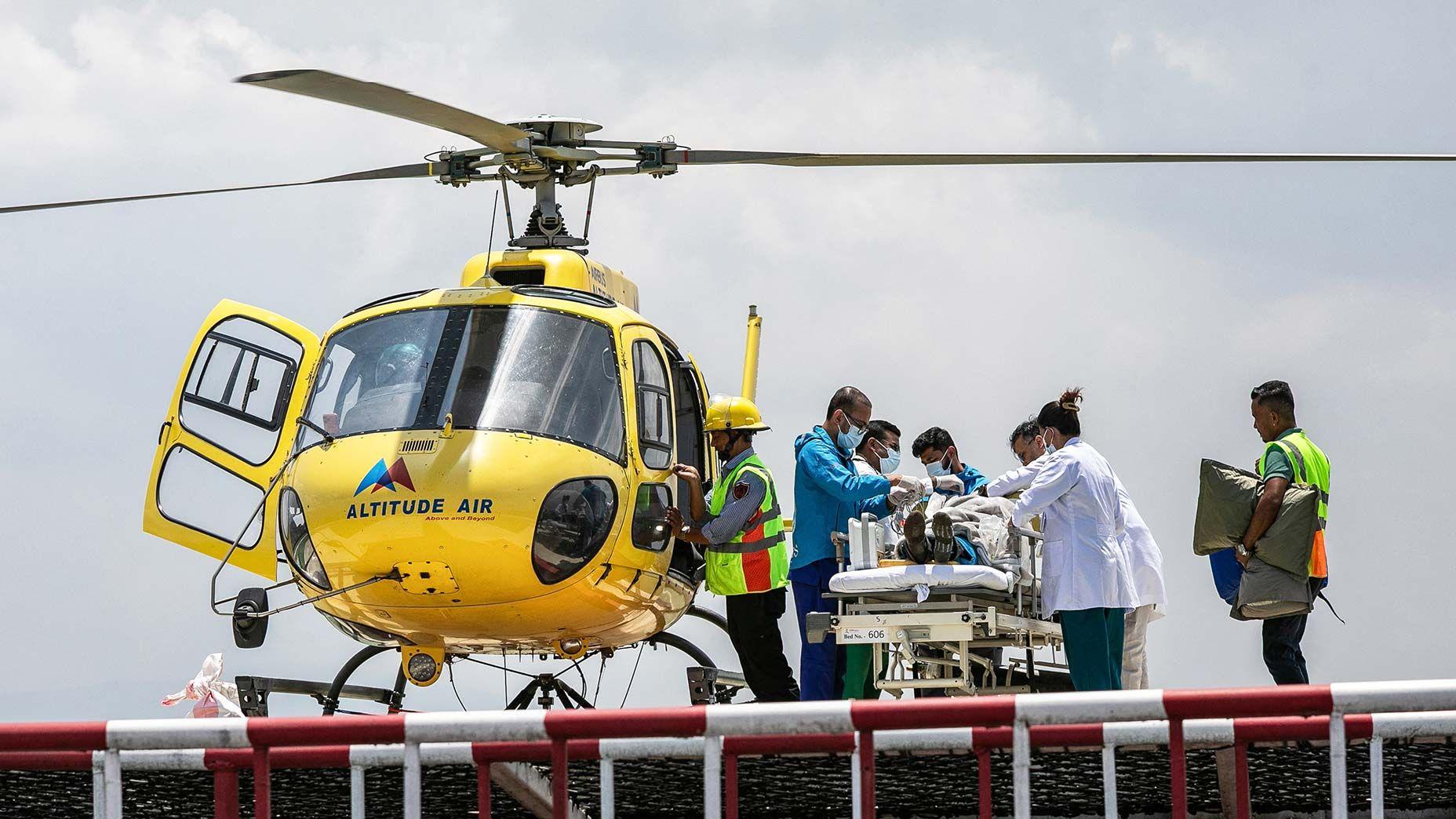 Personal médico atiende a Dawa Sherpa, un guía de escalada del Everest, mientras se preparan para trasladarlo por vía aérea a un hospital a bordo de un helicóptero amarillo.
