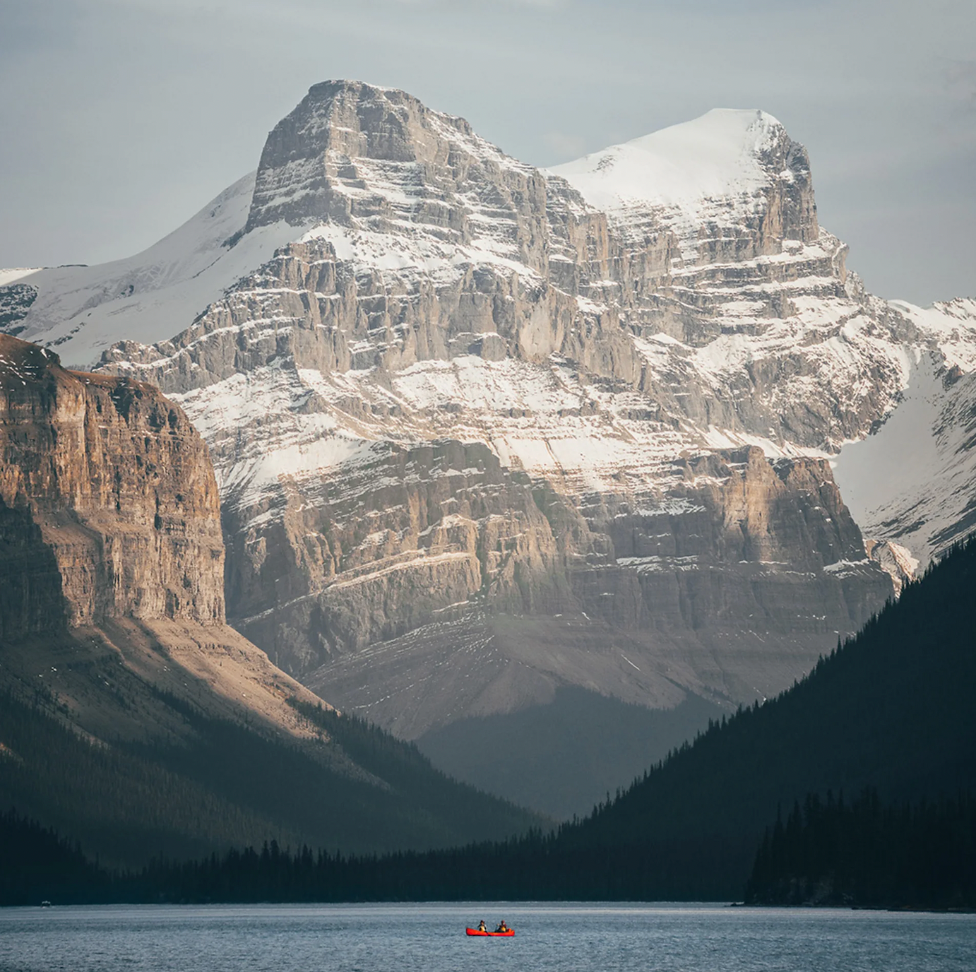 거대한 설산이 호수를 내려다보는 가운데 붉은 카누 한 척이 물 위를 지나간다.