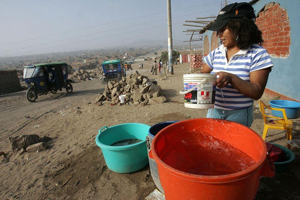 Una mujer junto a cubos de agua en una calle sin asfaltar de Perú. 