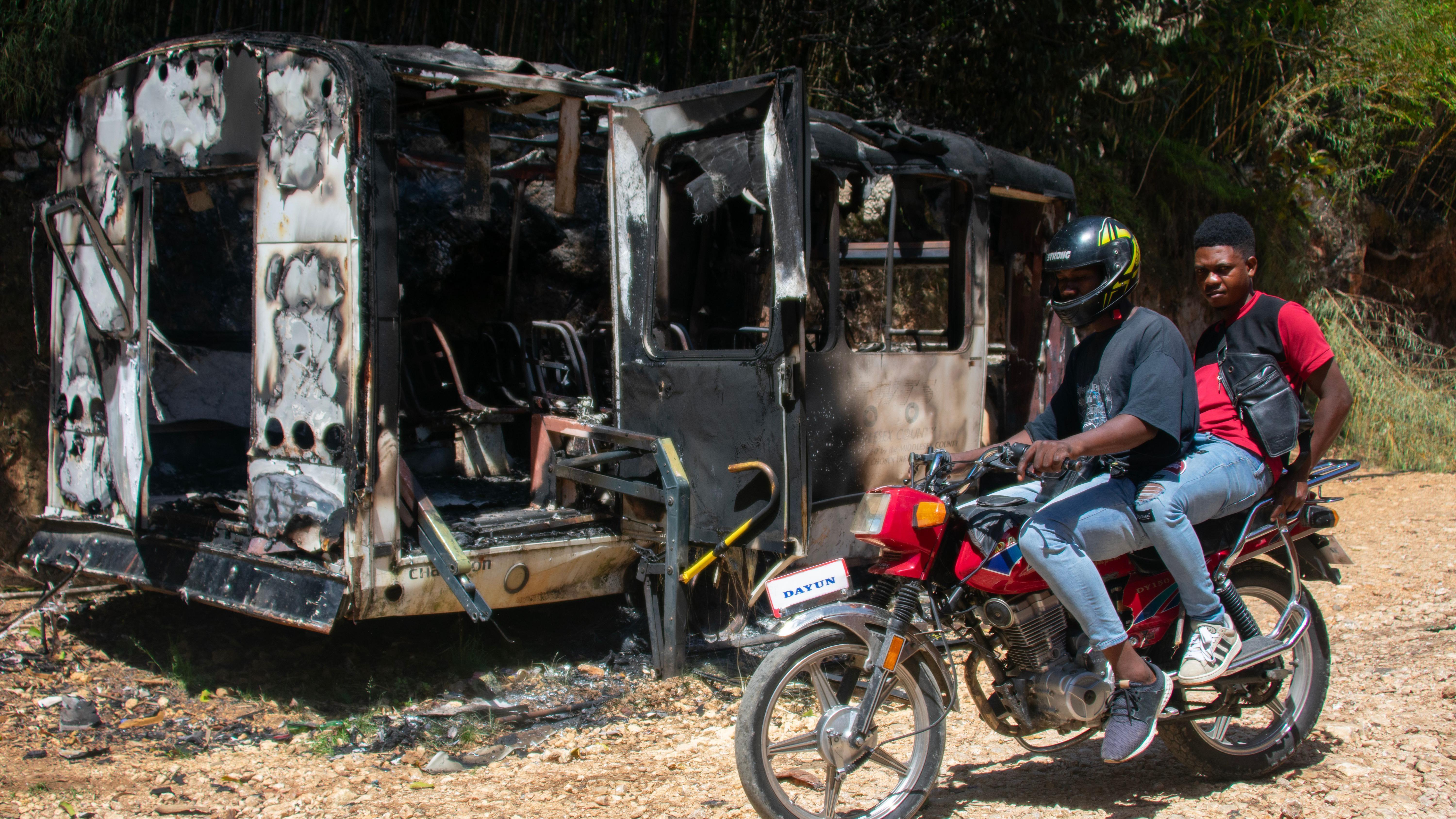 Unas personas en moto pasan junto a un vehículo calcinado en la zona de Kenscoff, Haití, el 24 de agosto de 2026.  