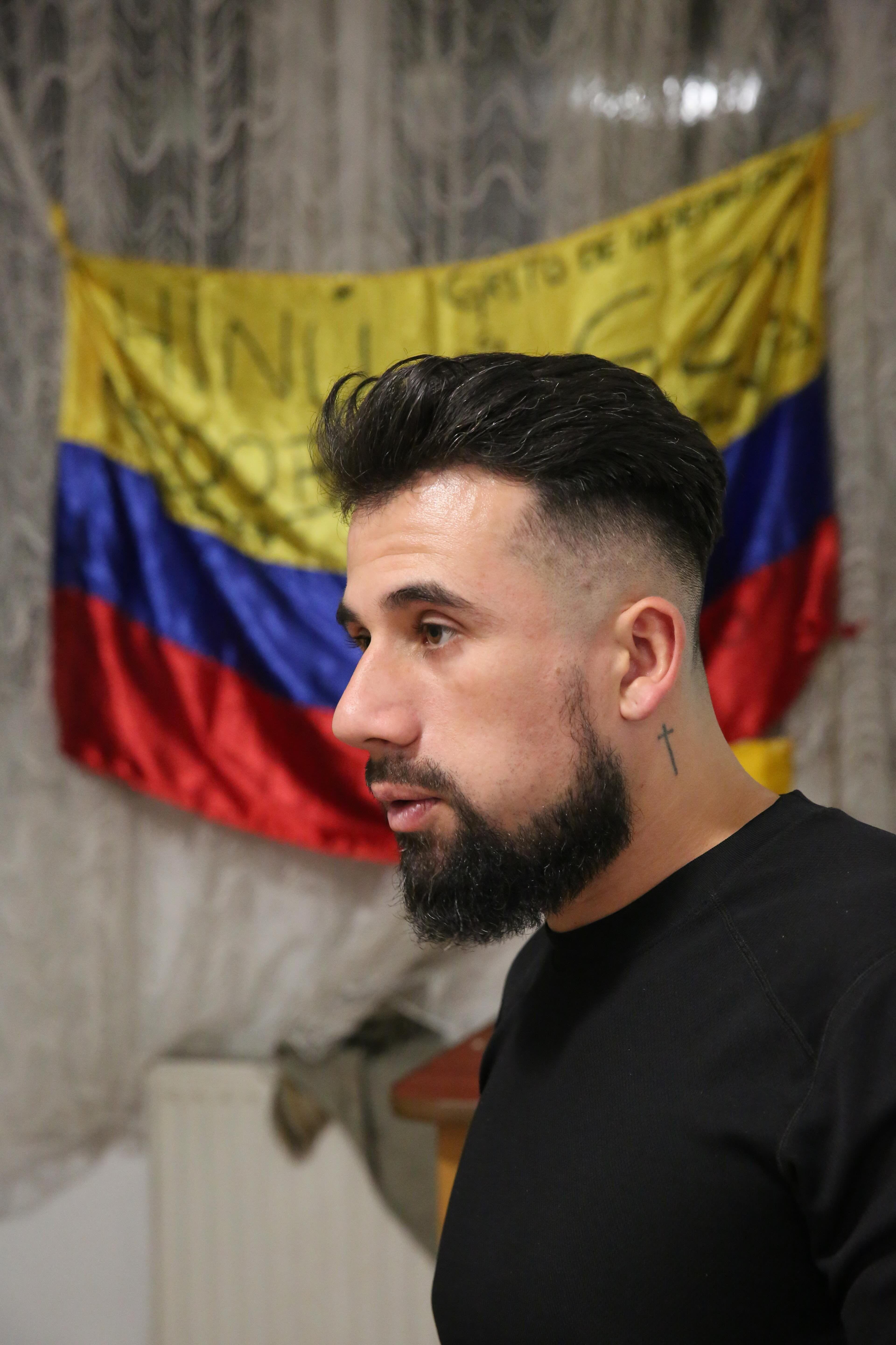Árabe está parado de perfil, con una bandera colombiana detrás de él.