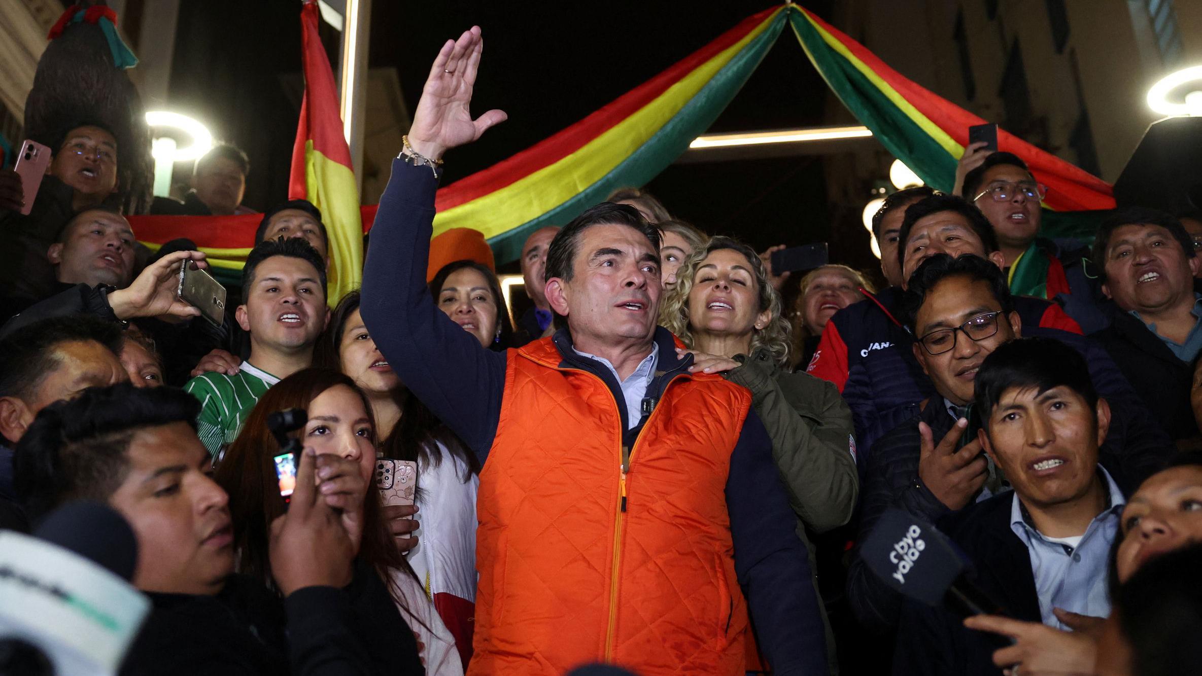 Rodrigo Paz con chaleco rojo yrodeado de partidarios levanta el brazo derecho