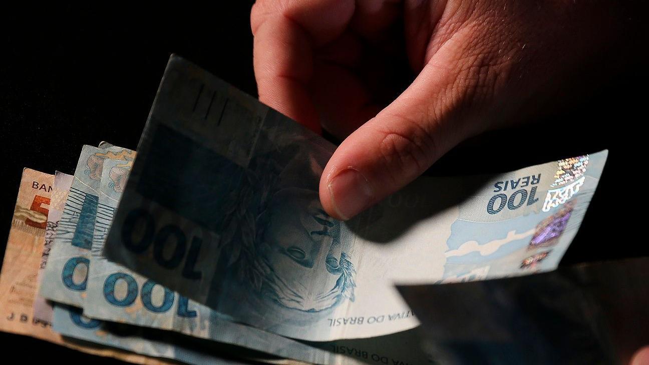 M&atilde;o segura nota de cem reais e a coloca sobre outras c&eacute;dulas