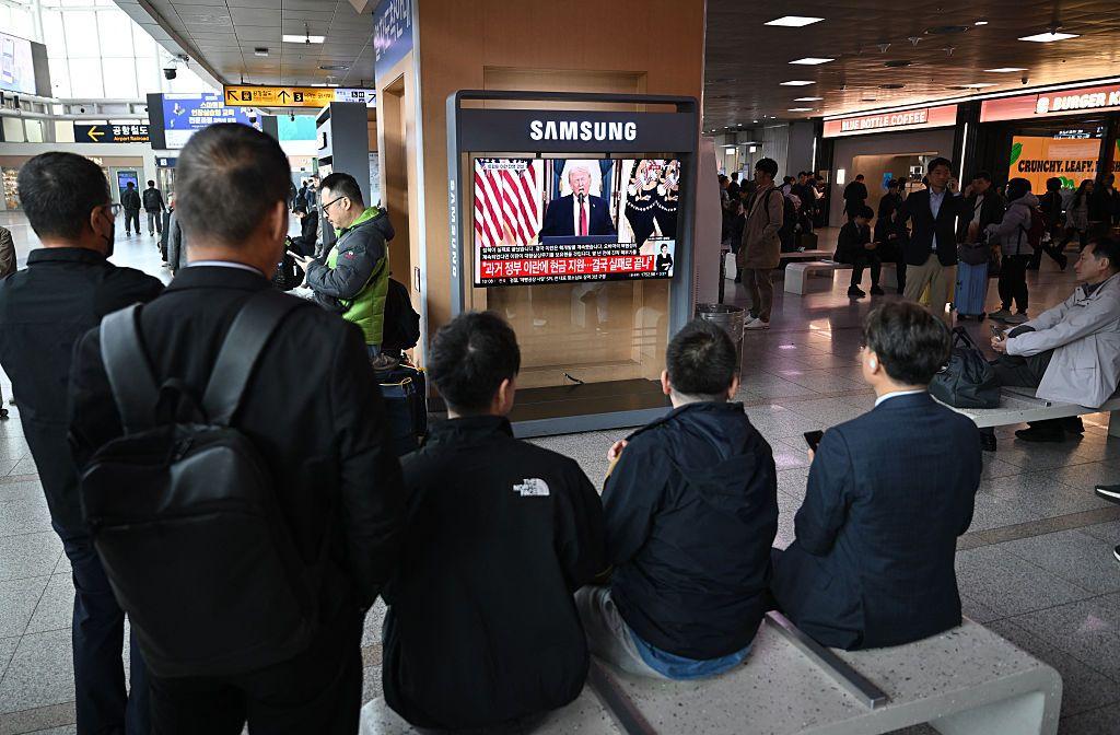 Transeúntes sentados en una banca de una estación de metro de Seúl, Corea del Sur, observan un televisor donde se transmite el discurso del presidente Trump