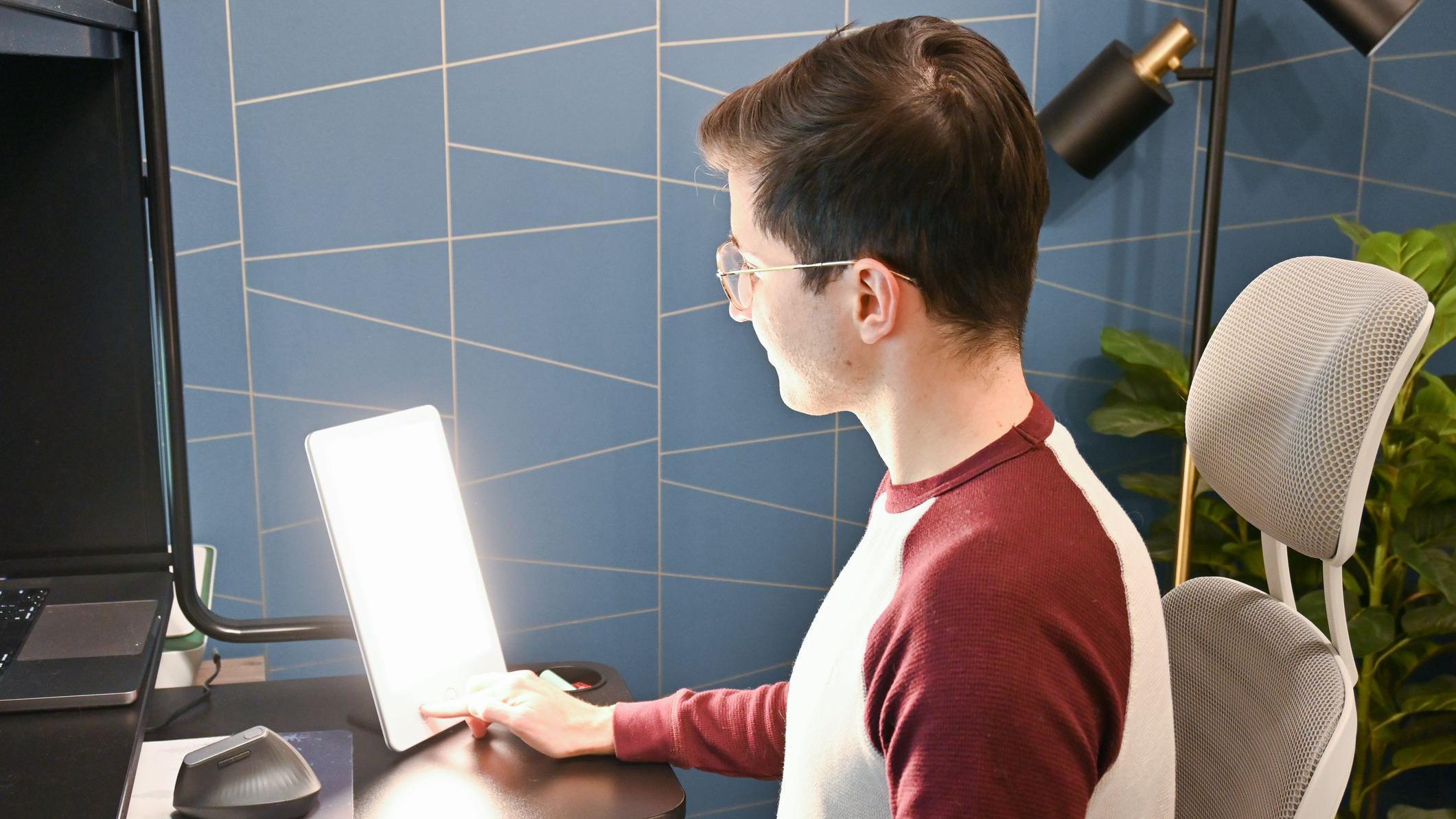 Jovem de &oacute;culos, sentado, olha para uma l&acirc;mpada usada para tratamento da depress&atilde;o sazonal