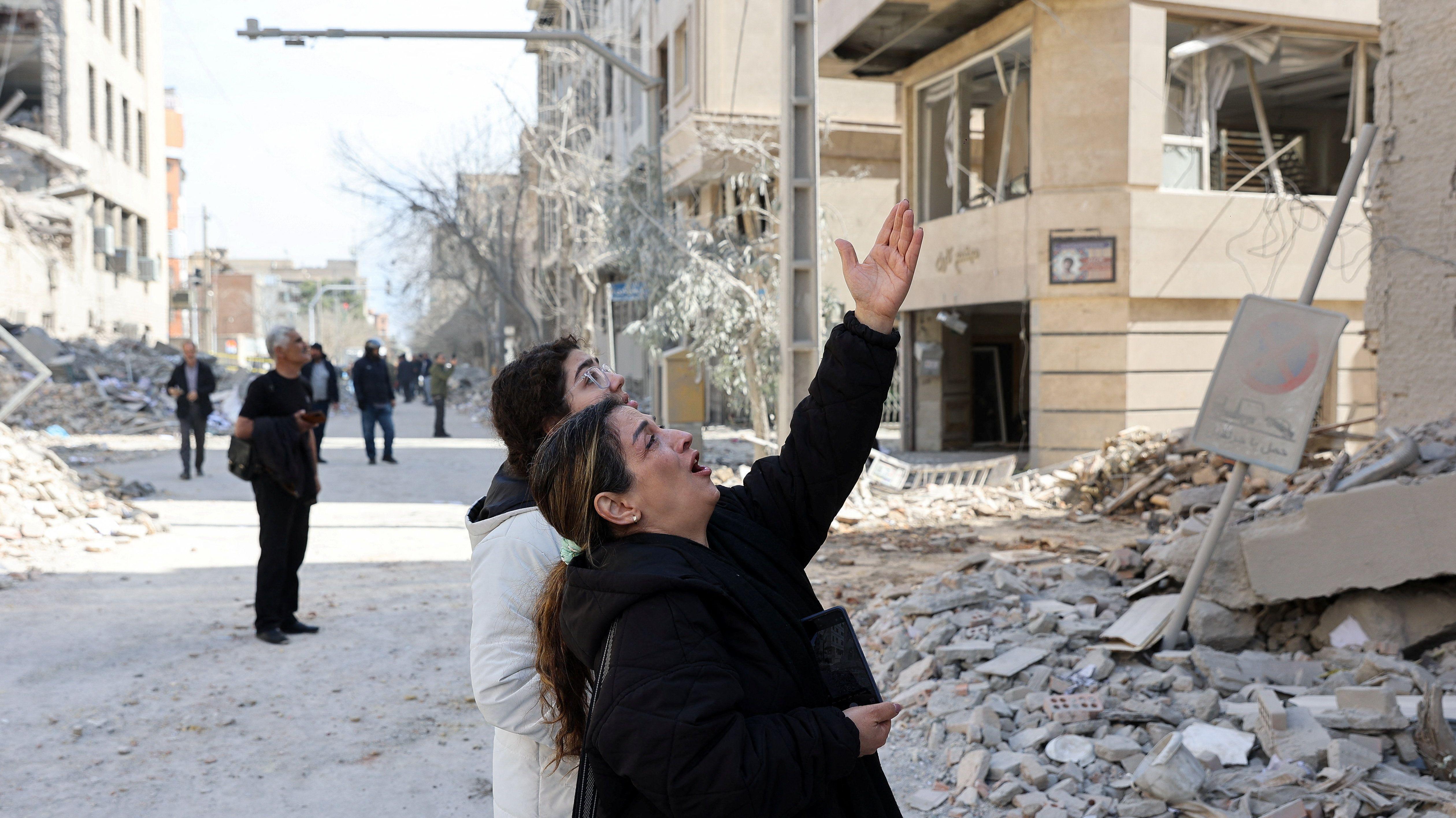 Žena i dečak gledaju i pokazuju rukom oko njih su razrušene zgrade