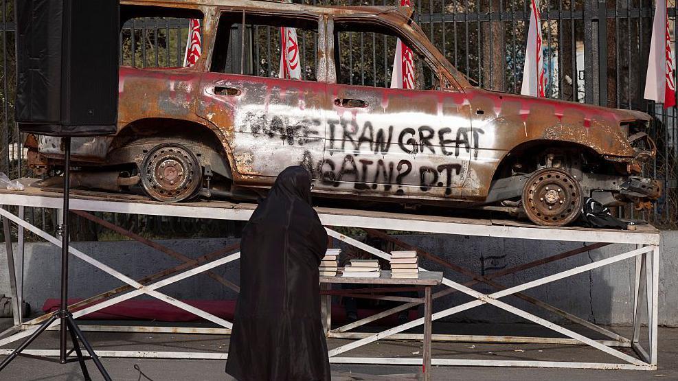 Una mujer iraní con chador se encuentra frente a una ambulancia destruida.