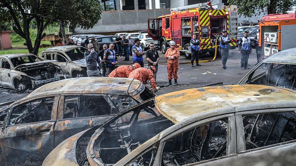 Bomberos y policías trabajan junto a vehículos quemados en el lugar del accidente de helicóptero en el barrio Recreio dos Bandeirantes en Río de Janeiro, Brasil, el 14 de junio de 2026.