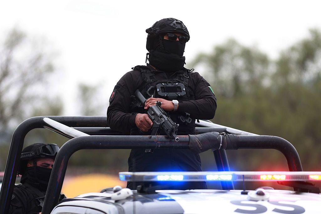 Un agente policial mexicano encapuchado de pie en un vehículo.