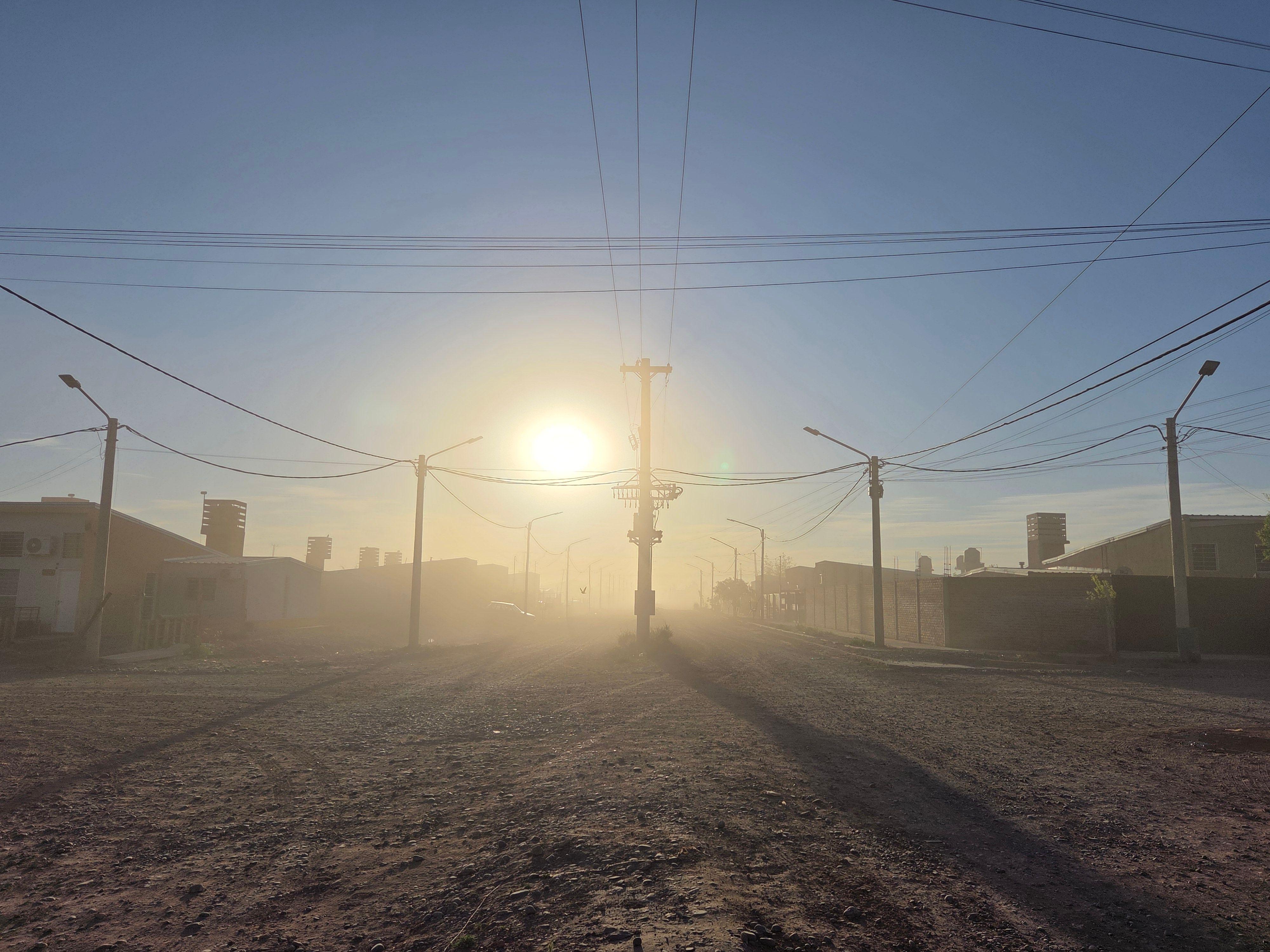 Calle de tierra, nube de polvo y el sol del amanecer.