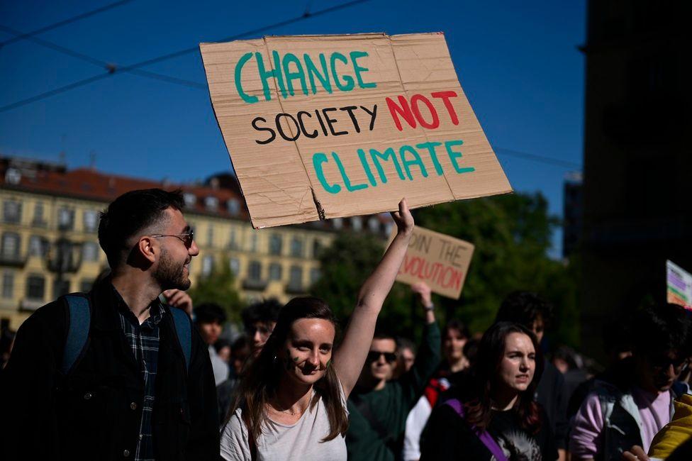 Varios jóvenes en una manifestación. Una de las participantes levanta una pancarta que dice: Change society No climate.